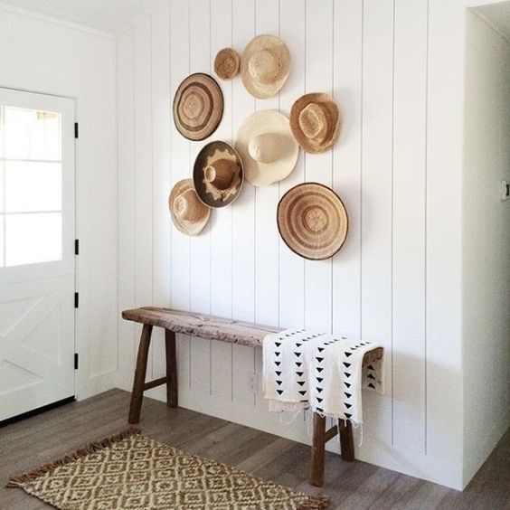a simple entryway with a rough wooden bench and a white shiplap wall highlighted with decorative baskets and hats