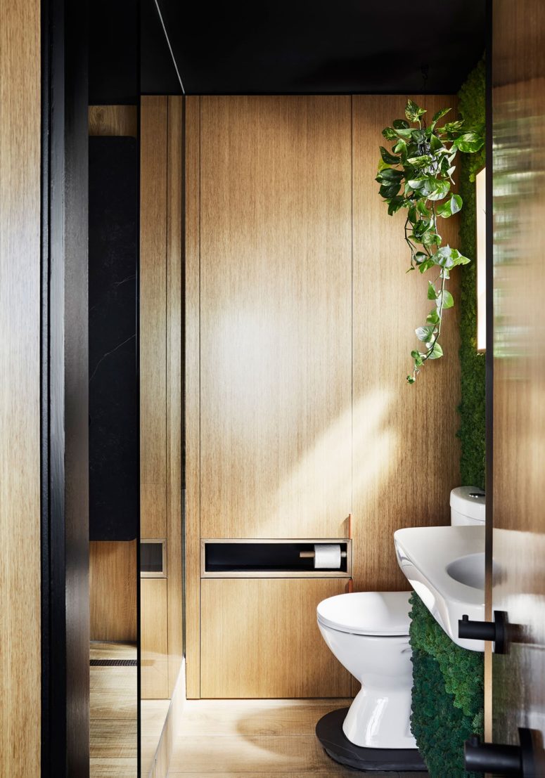 The bathroom features a shower and much light-colored wood and black surfaces to continue the color scheme of the apartment