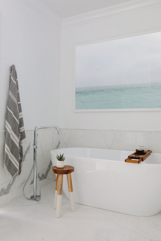 a fresh and airy bathroom done in white and creamy shades, with light greys and an aqua artwork showing the sea