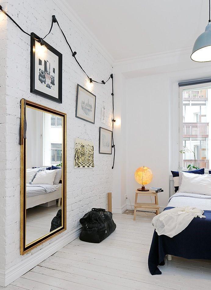 A dreamy Scandinavian bedroom with white brick walls, a whitewashed floor shows off black framed art and dark bedding