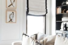12 white Roman shades with a black border add chic and interest to the monochromatic living room