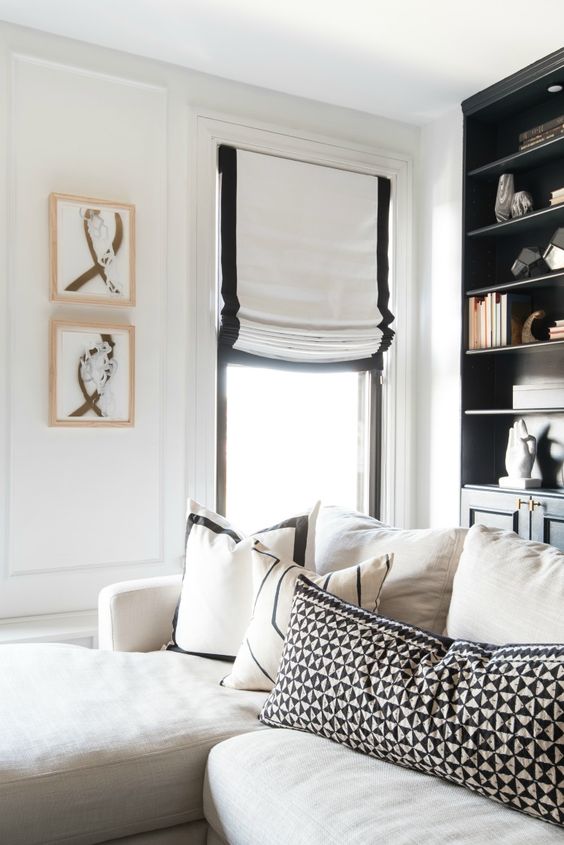 white Roman shades with a black border add chic and interest to the monochromatic living room