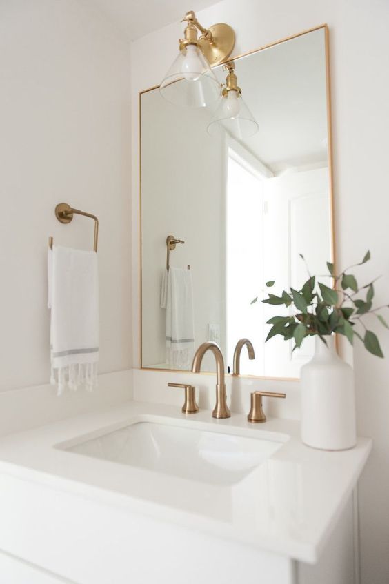 a mirror in a thin gold frame, with gold fixtures and a wall lamp for a stylish and bright bathroom nook