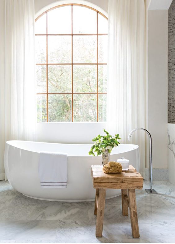 A contemporary bathroom with a free standing bathtub and a rough wooden stool