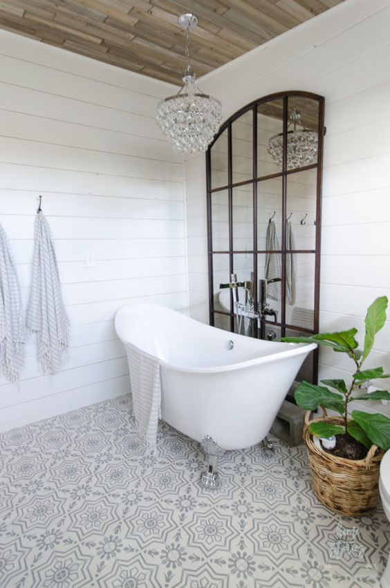 a glam farmhouse bathroom done with white shiplap, mosaic tile floors and a crystal chandelier plus a framed mirror