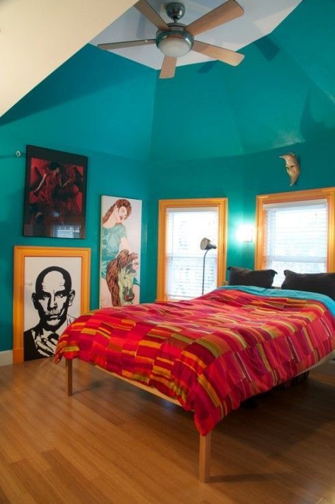 a turquoise bedroom is accented with red bedding and bright yellow framing of the windows