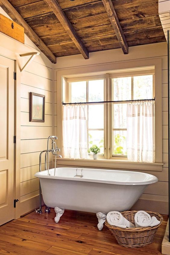 a small farmhouse bathroom in earthy tones, a wooden floor, sandy shiplap on the walls and a basket for towels