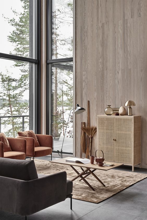 a warm-colored and neutral living room done with wood, cane and leather plus gorgeous views from double height windows