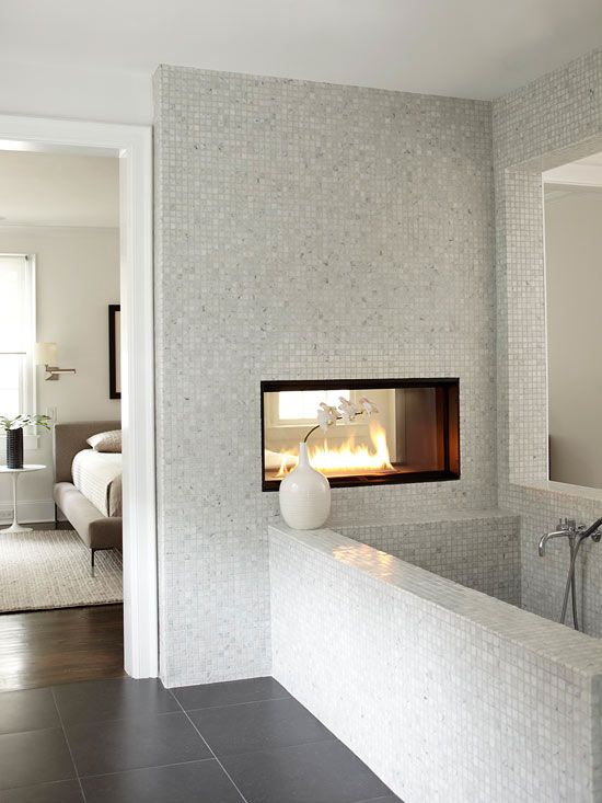 a contemporary bedroom and bathroom separated with a wall with a fireplace