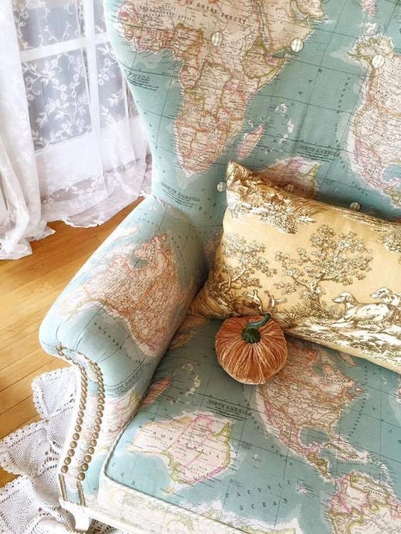 a map covered wingback chair with decorative nails detailing, a vintage pillow and a velvet pumpkin is very whimsy