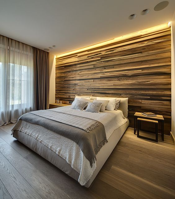 a weathered wood clad statement wall with strip lighting on the top gives you light for reading and accents the bed