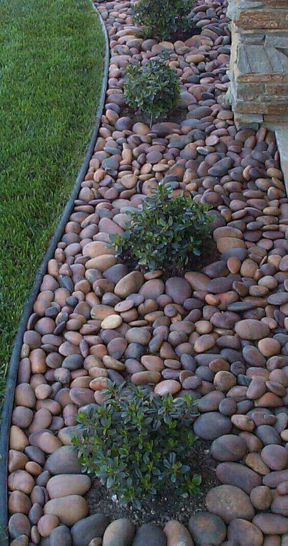 chic and bold pebble garden edging with little greenery bushes growing inside it for a fresher and cooler look