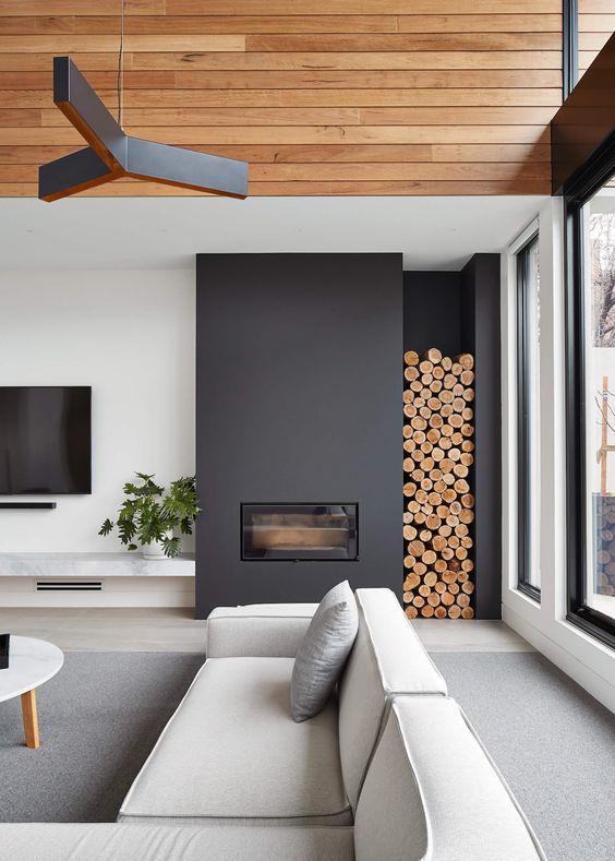 a contemporary living room done with a black sleek fireplace and firewood storage plus a black chandelier