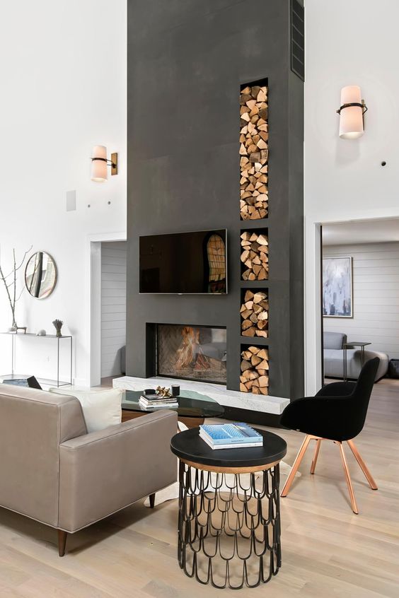 A contemporary living room with contrastign features   a tlall matte black wall with a fireplace and firewood storage plus a black chair