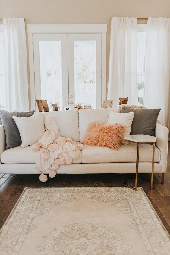 creamy, pink and green pillows in various fabrics, a fluffy pink fur pillow and a pink blanket with pompoms for a cozy feel