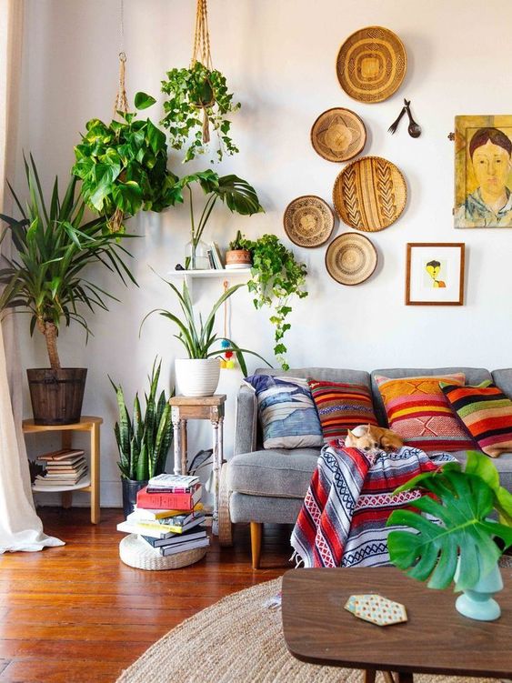 decorative baskets on the wall, many potted plants, colorful printed pillows and a blanket make up a cool boho space