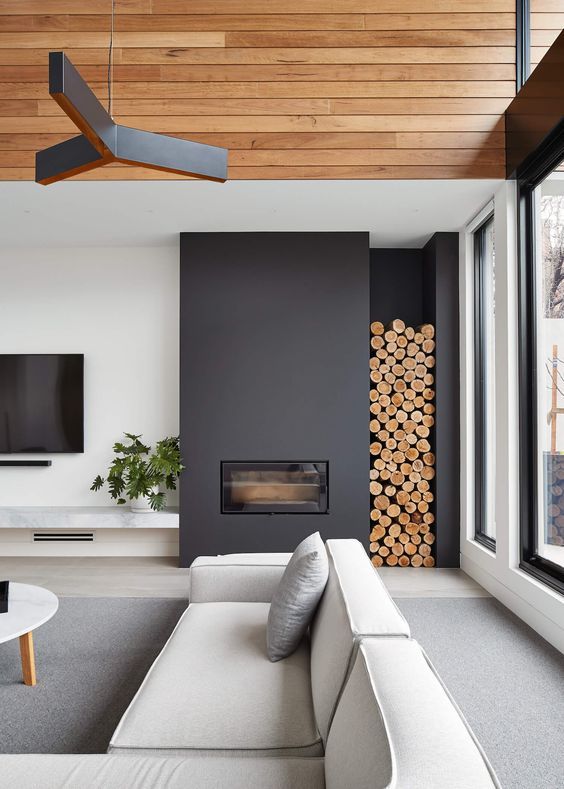a minimalist black fireplace with firewood storage by it brings coziness to the space