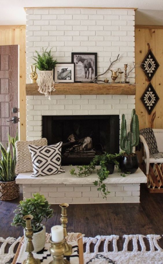a brick clad fireplace with a wooden mantel, potted plants, pillows and artworks for a boho living room