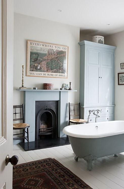 a vintage fireplace clad with blue and a mathcing tub and storage piece create a welcoming vintage bathroom