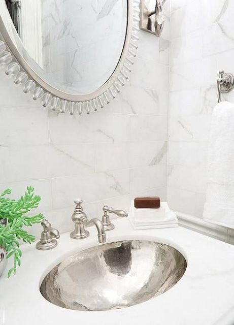 a Calcutte marble countertop with a silver hammered sink, matching marble tiles around and a mirror in a silver frame