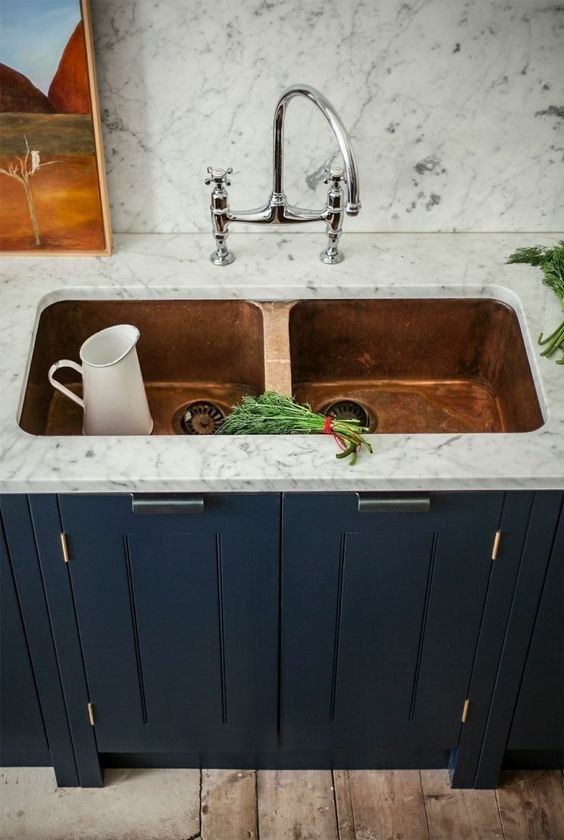a gorgeous double copper sink in a white stone countertop look chic, especially with a navy cabinet