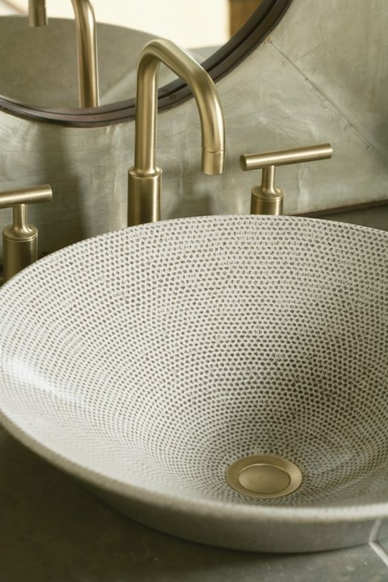 a large round sink with hand painting creates a feeling of a texture and brass touches make it look brighter and bolder