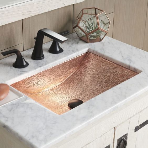 a white marble bathroom vanity with a hammered copper sink and matte black fixtures for a chic and glam look