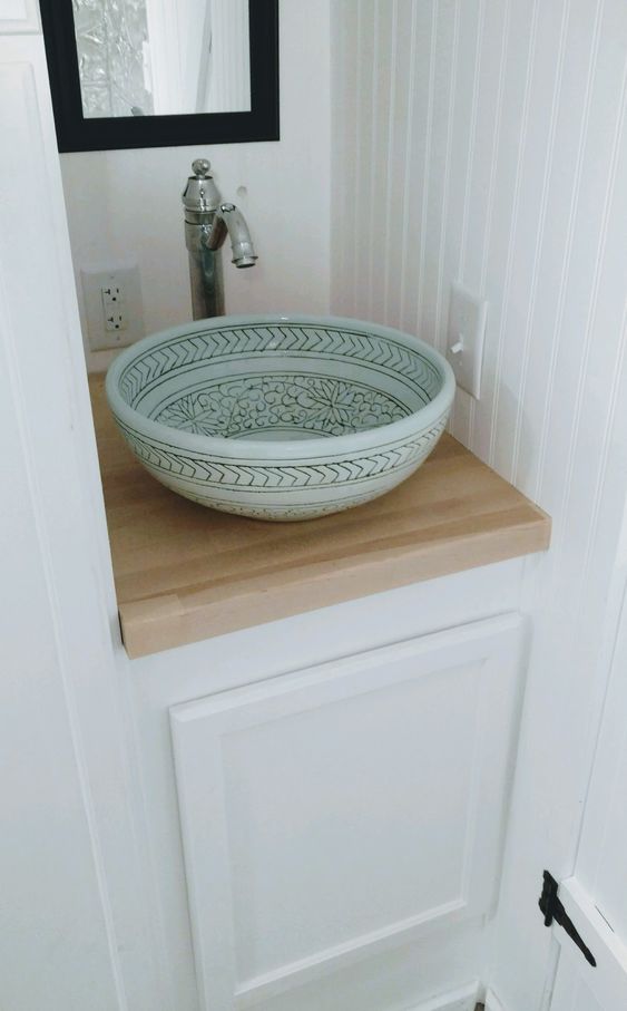 An aqua colored vessel sink with hand painting adds a subtle touch of color and a vintage faucet is a perfect match