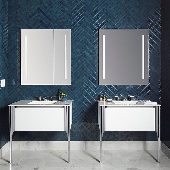 a bold contemporary bathroom wih teal skinny tiles clad in a chevron pattern and contrasting white vanities