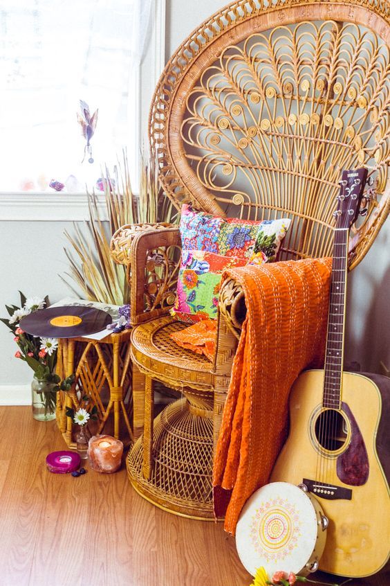 A colorful free spirited nook with a peacock chair, bright textiles, a rattan side table, blooms and some musical instrument
