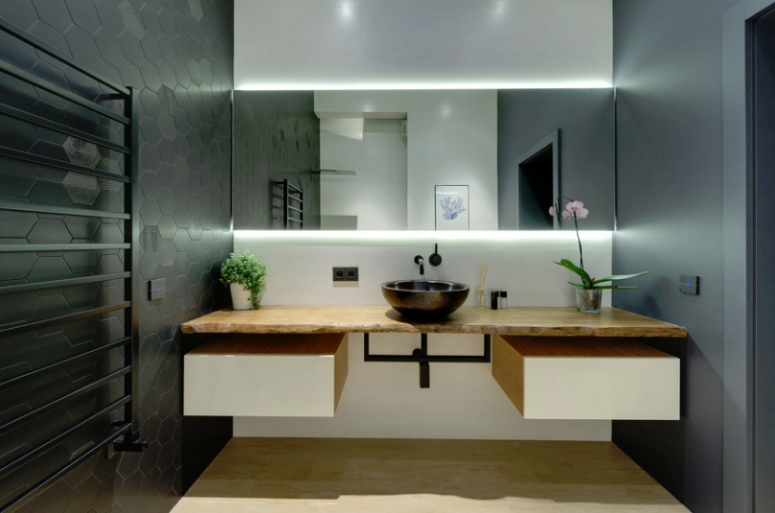 The bathroom is done with black hex tiles, sleek concrete walls, a floating vanity with storage and a lit mirror