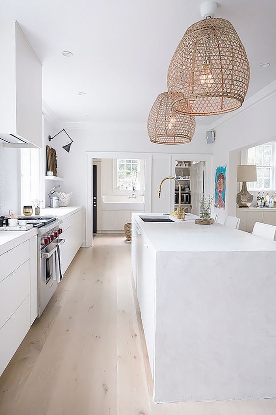a pure white kitchen is given a rustic and outdoor feel with rattan lampshades over the kitchen island