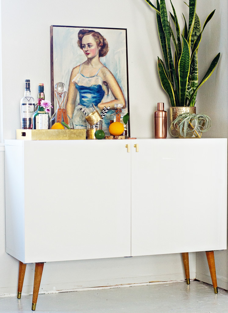 A stylish home bar in mid century modern style is made of an IKEA Besta unit on legs, everything is hidden inside for kid proofing