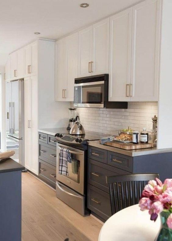 a two tone kitchen in navy and white with a white skinny tile backsplash and metal countertops for a bright and chic look