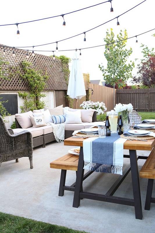 a patio seamlessly flowing into a dining space with a table and benches plus lights all over the space