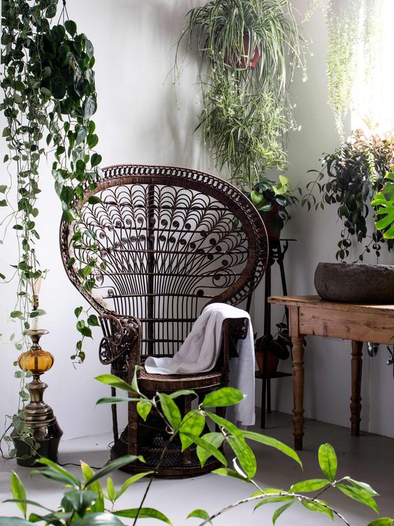a dark stained peacock chair in a nook with potted greenery, a wodoen table and a Moroccan decoration for a boho feel