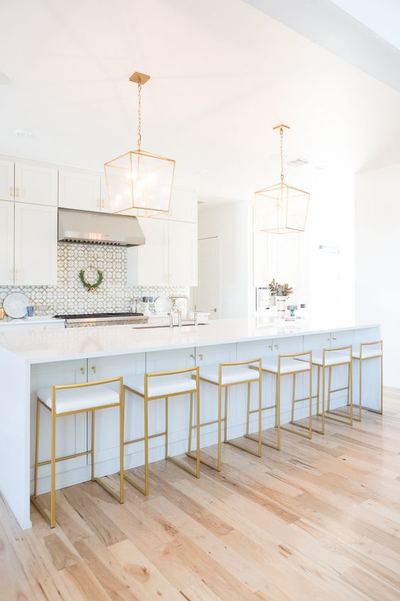 very elegant gold stools with white seats highlight the kitchen design and echo with the pendant lamps