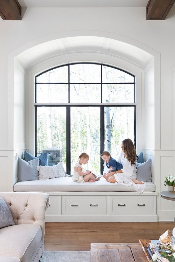 an arched window features an upholstered bench, some drawers and pillows for storage