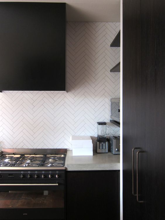 a dark minimalist kitchen done with concrete countertops and white skinny tiles clad in a chevron pattern for a catchy look