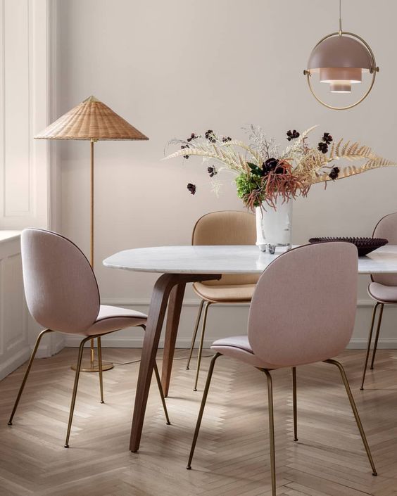 An elegant mid century modern dining space with blush chairs and a wicker floor lamp to add a relaxed feel to the room