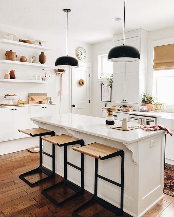 bold dark metal and light-stained wood stools add a touch of drama to the neutral kitchen and pendant lamps continue that