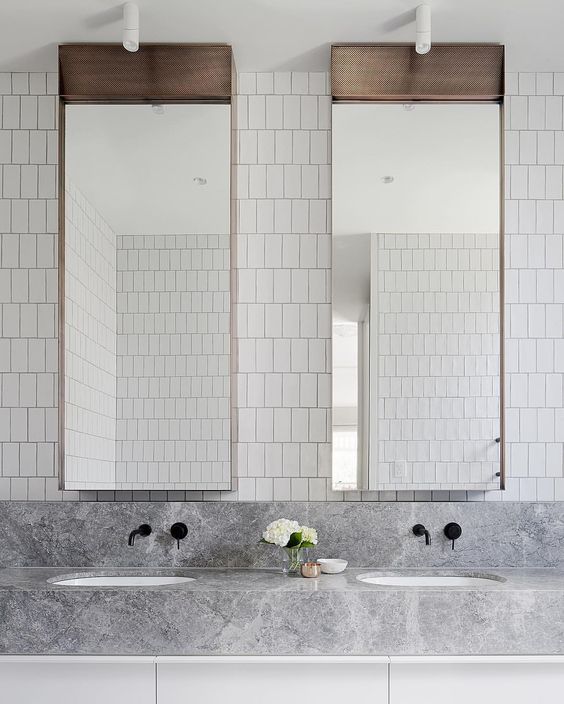 a minimalist sink space with white skinny tiles on the wall, catchy mirrors, a grey marble vanity