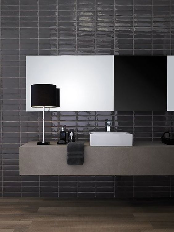 a moody bathroom with black skinny and shiny tiles on the wall and a concrete floating vanity for a contrast