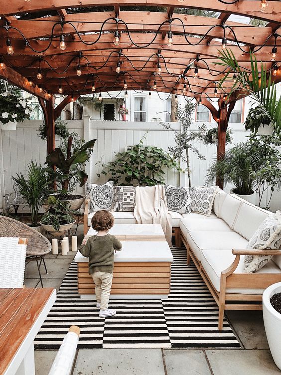 a boho chic patio finished off with a striped rug, potted greenery, printed pillows and lights