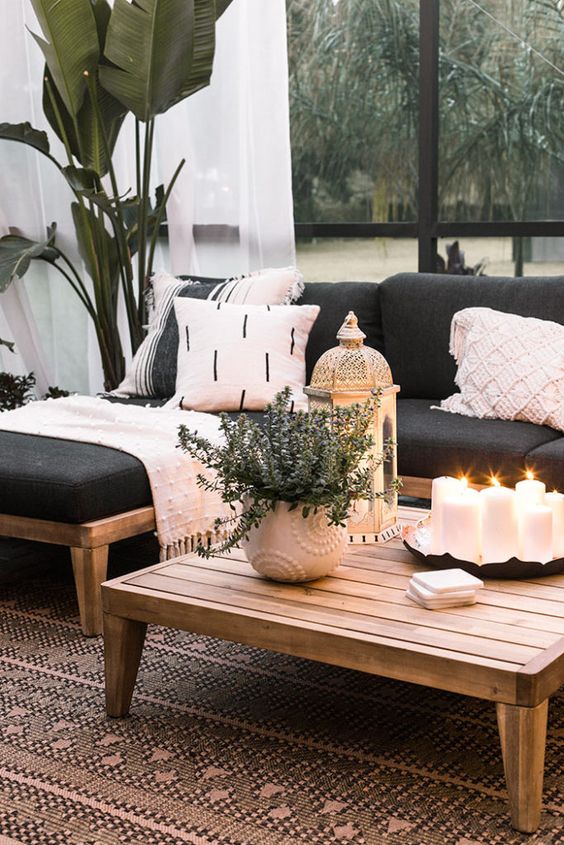 a chic patio decorated with contrasting blankets and pillows, candle lanterns and potted greenery