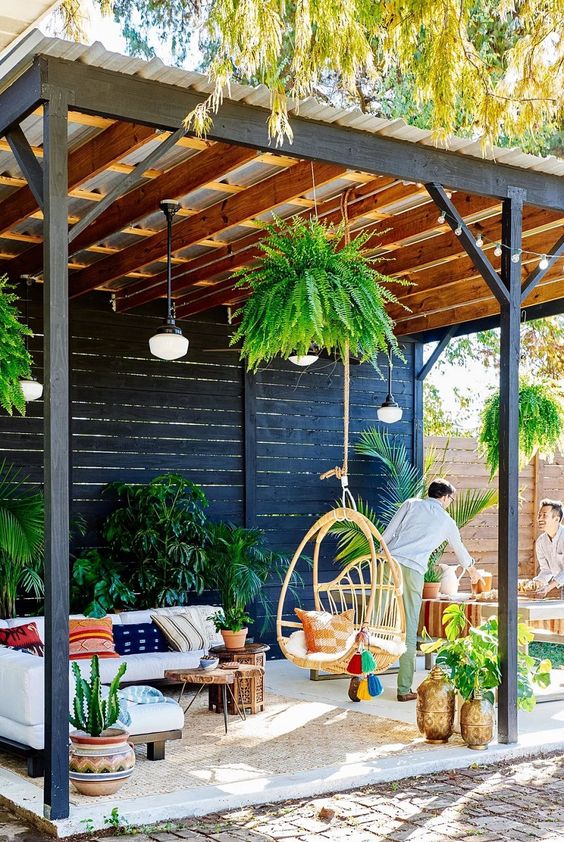 a bright patio with potted greenery, colorful pillows, a hanging rattan chair and pendant lamps