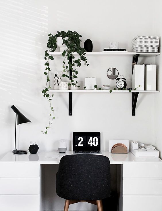 A Scandinavian home office nook with a white desk, a black chair, lamp and some wall mounted shelves