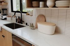 a Scandinavian kitchen with stained and white cabinets, white stone countertops, a white skinny tile backsplash and black handles