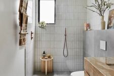 a beautiful grey bathroom with skinny and large scale tiles, a floating vanity, a shower space, a wooden stool and copper fixtures