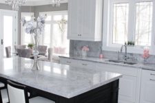 a black kitchen island and white cabients are covered with the same neutral stone countertops for a cohesive look